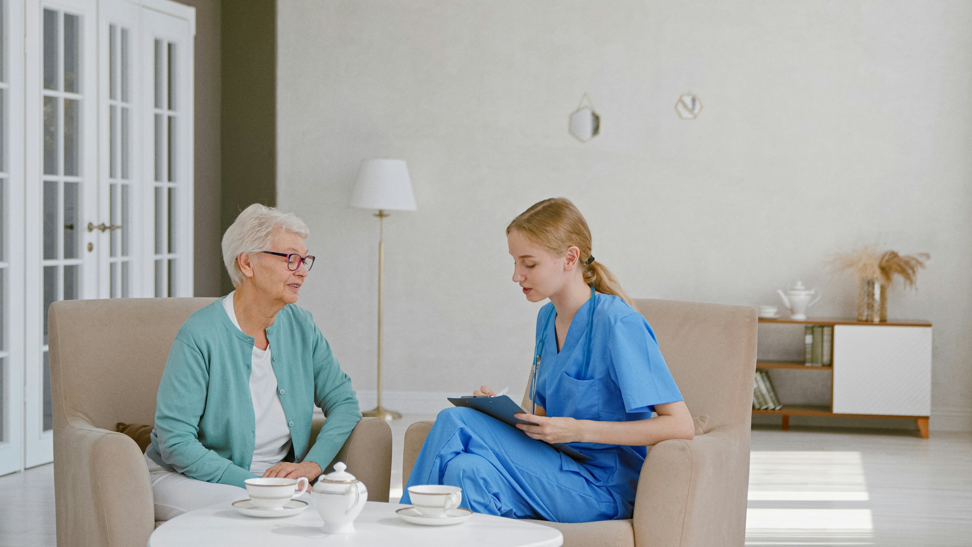 Senior woman with short haircut talks to young female doctor writing notes on clipboard